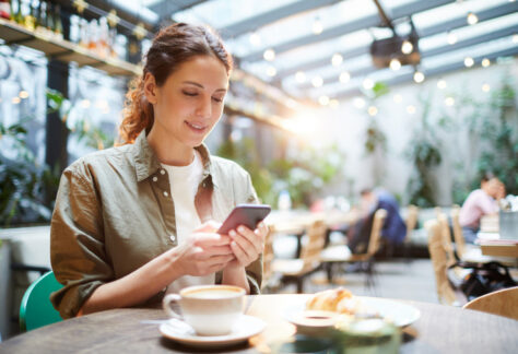 Woman using mobile phone to make a digital payment at a café, representing convenient mobile bill pay and payment preferences